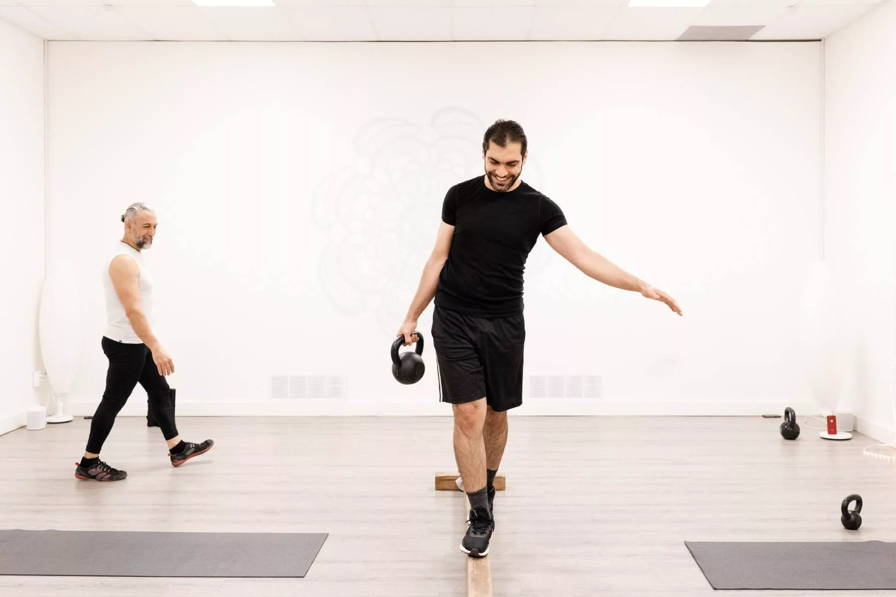 man in fitness class walking across balance beam with kettlebell in hand