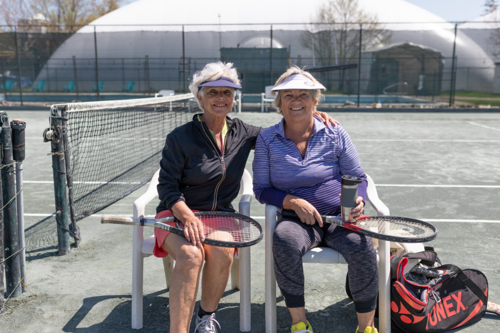 two older women with summer tennis pass sitting on outdoor clay court in ottawa