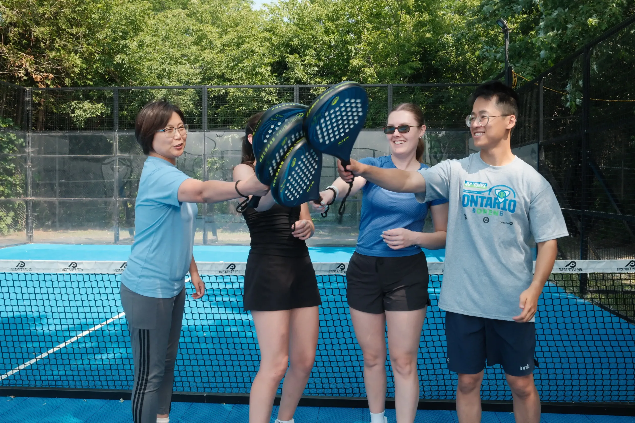Group of men and women laughing on the outdoor padel court at Rideau Sports Centre
